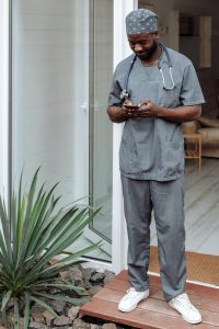 Medical professional in grey scrubs and cap, holding a phone